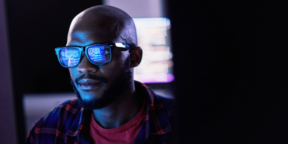 A man looking at a computer screen with the screen reflecting on his glasses.