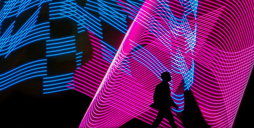 Silhouette of person walking with a colourful background behind them.