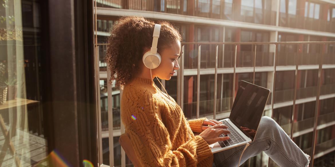 Woman sitting on balcony with laptop on knees