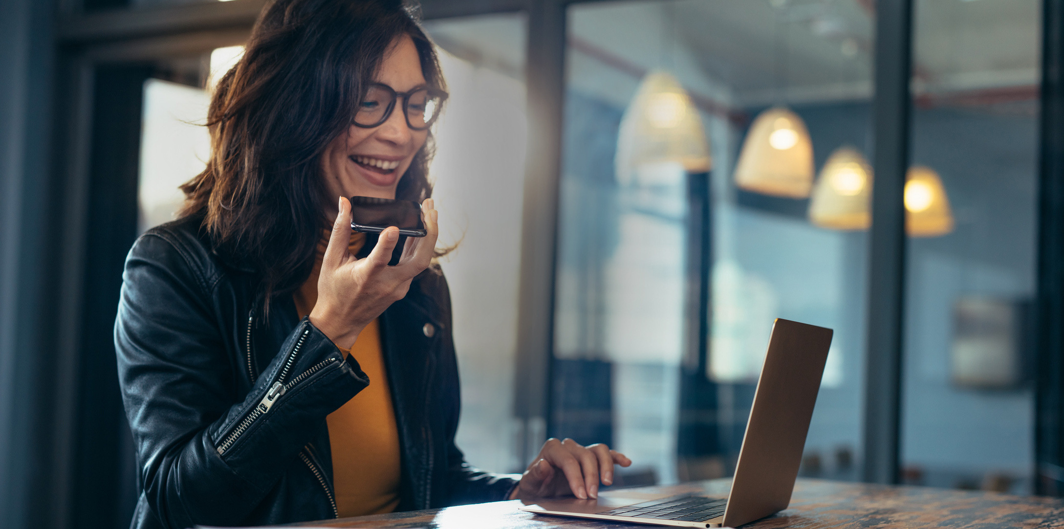 Woman on laptop, smiling, speaking in mobile phone.