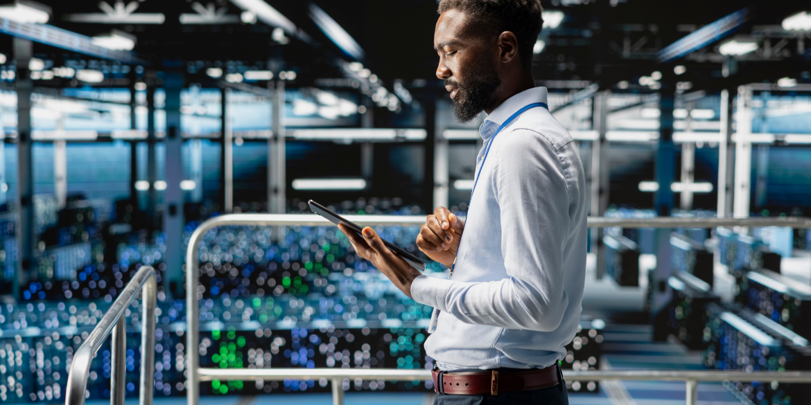 Man using a digital device in a large server room or somewhere similar.