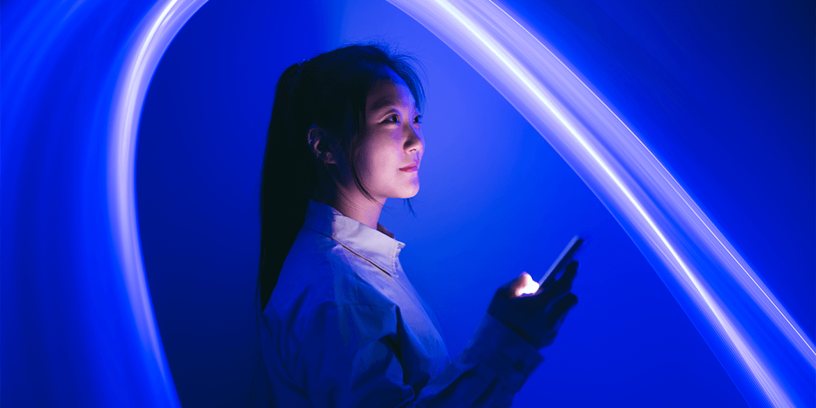 Man standing up leaning against wall looking at laptop.