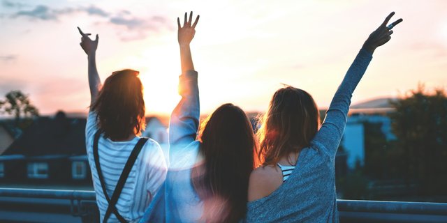 Three women raising hands up to the sunset