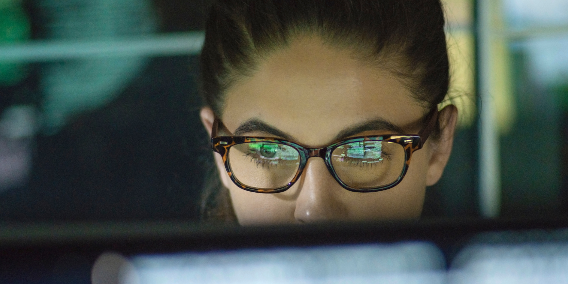A woman looking at a computer screen with the screen reflecting on her glasses.